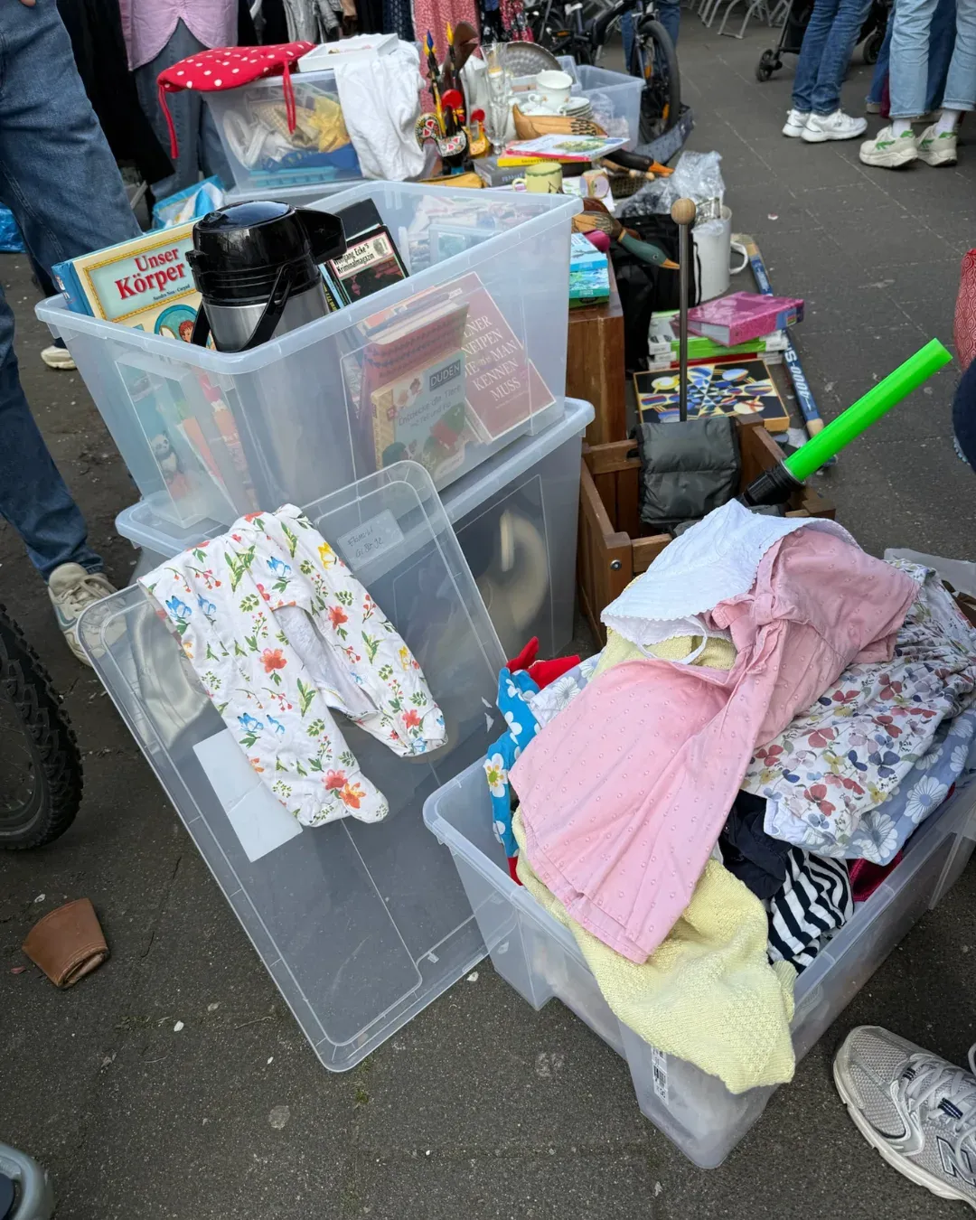Durchsichtige Kisten mit Büchern, Thermoskanne und Kinderkleidung auf dem Gehweg