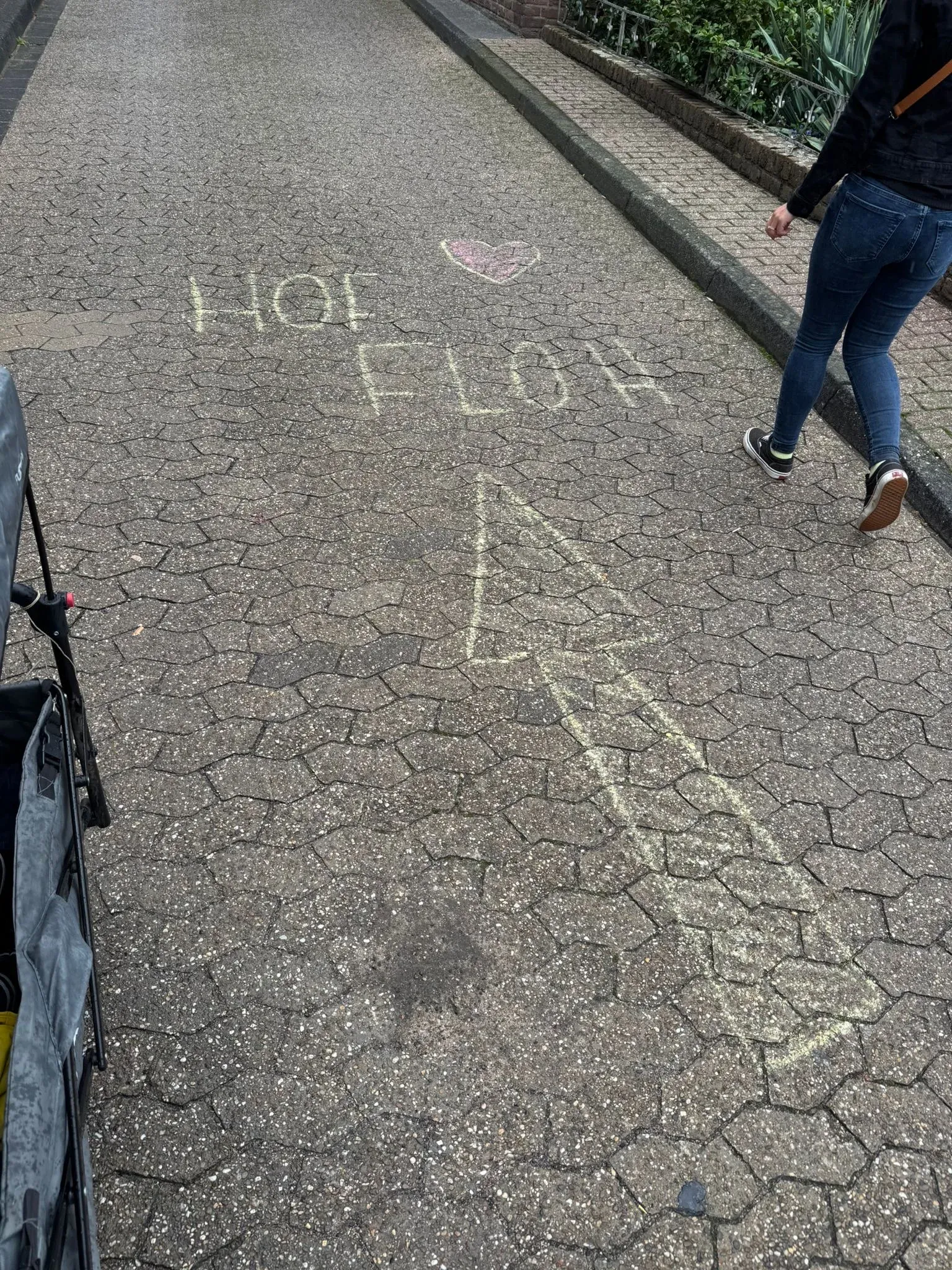 Kreidepfeil und „Hof Floh“ mit Herz auf einem Gehweg, daneben eine Person in Jeans