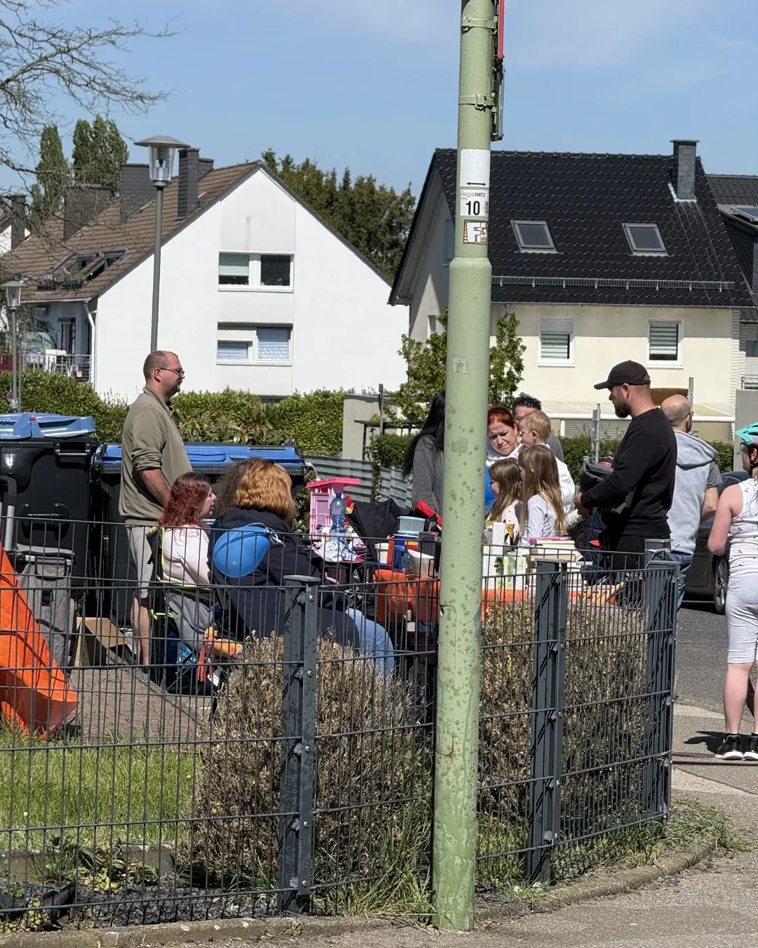 Menschen an einem Stand in einem eingezäunten Vorgarten an einer Straßenecke