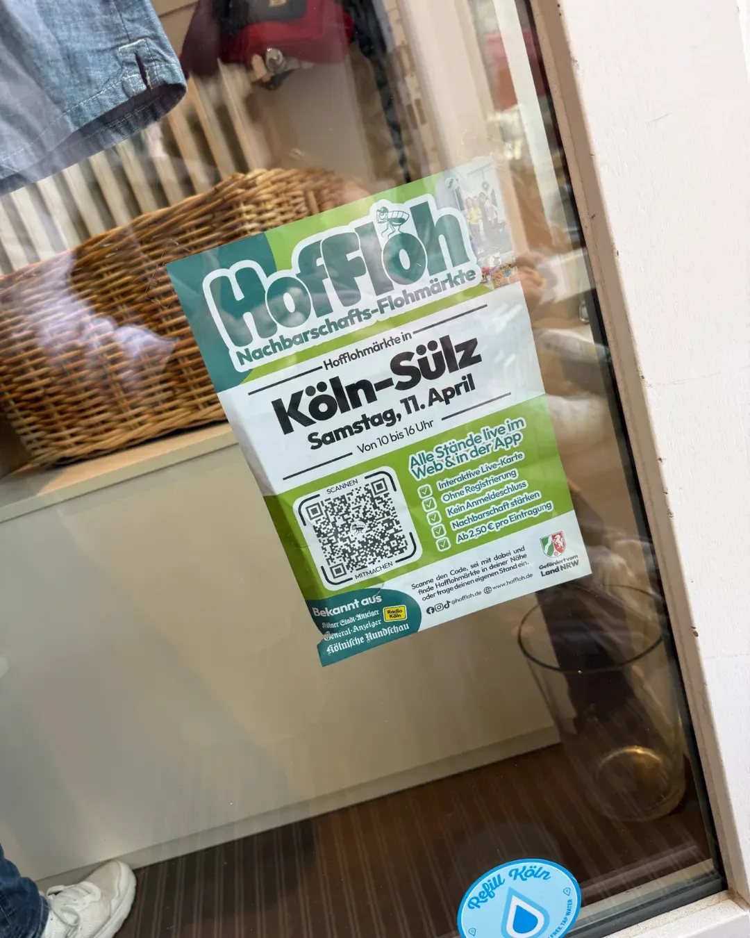 HofFloh-Plakat „Hofflohmärkte in Köln-Sülz, Samstag, 11. April“ in einem Schaufenster