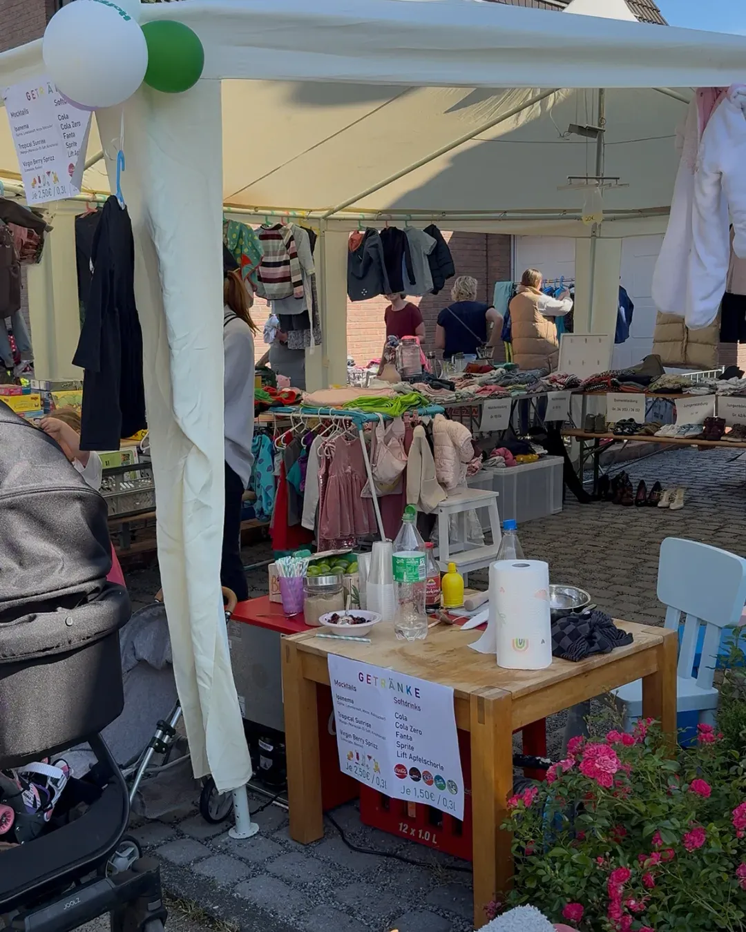 Pavillon mit Kinderkleidung und Schuhen, davor ein Tisch mit Getränkekarte