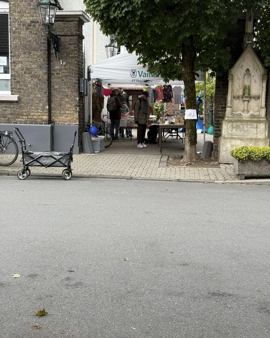 Stand unter einem Pavillon mit Kleidung in einer Hofeinfahrt, davor ein Bollerwagen an der Straße