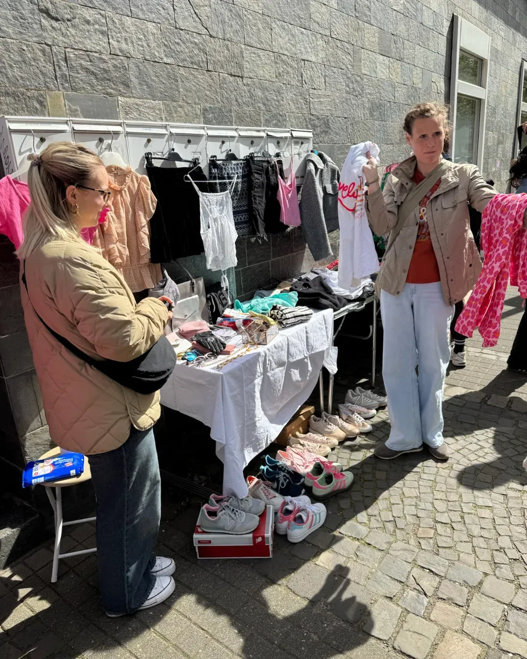 Zwei Frauen an einem Stand mit Kleidung auf Bügeln und Sneakern auf dem Pflaster