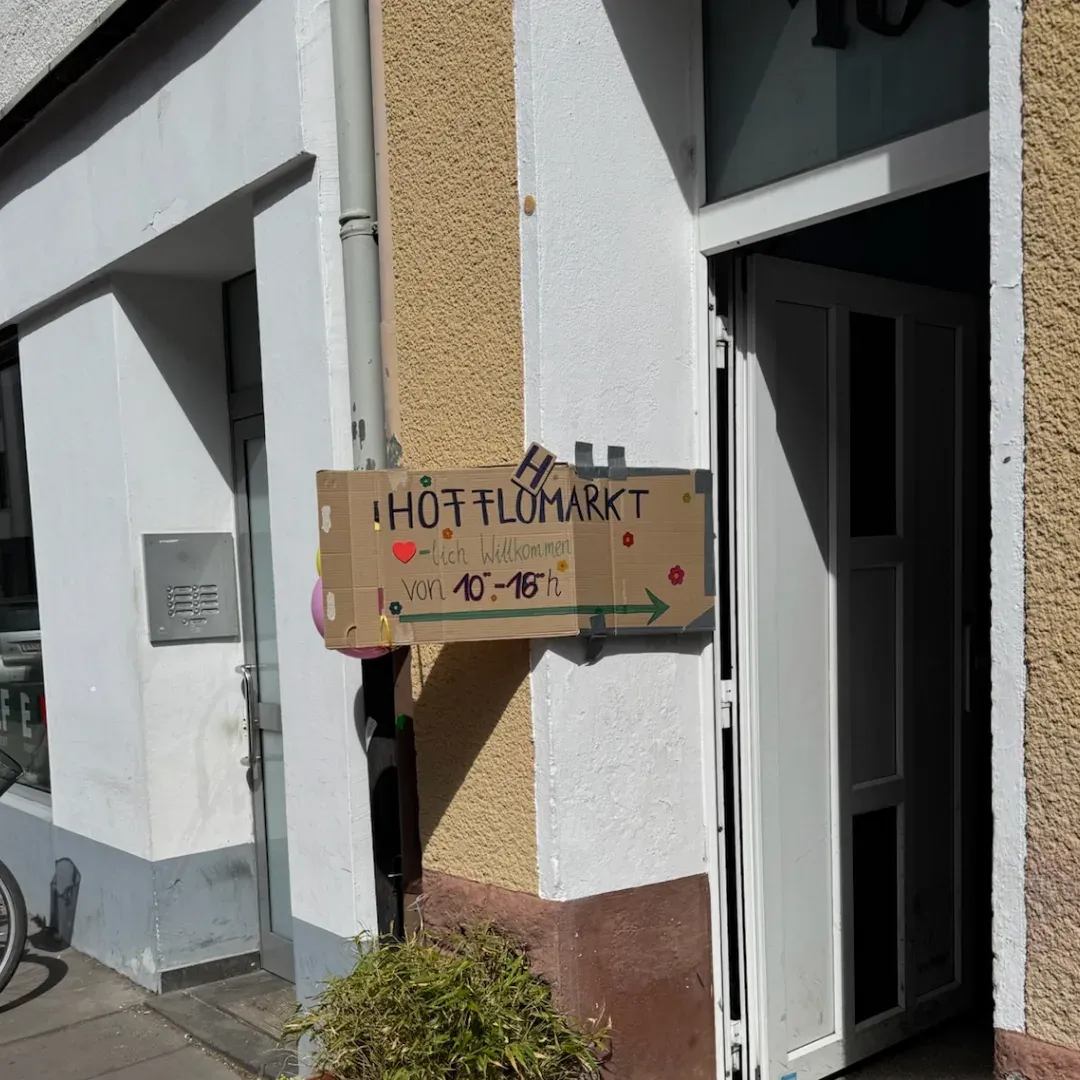 Pappschild mit „Hofflohmarkt“, Herz und Pfeil an der Hauswand neben einer offenen Haustür