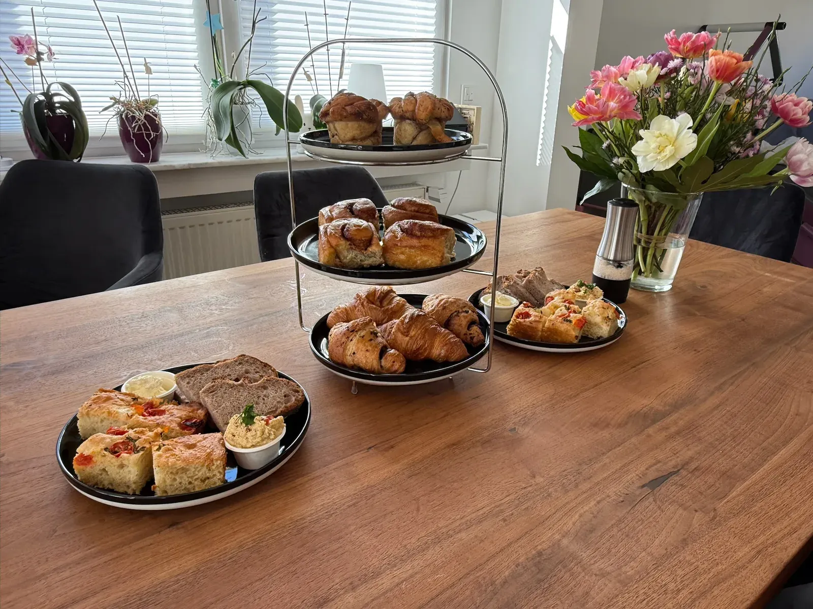 Frühstückstisch mit Etagere voller Croissants und Zimtschnecken, Focaccia und einem Tulpenstrauß