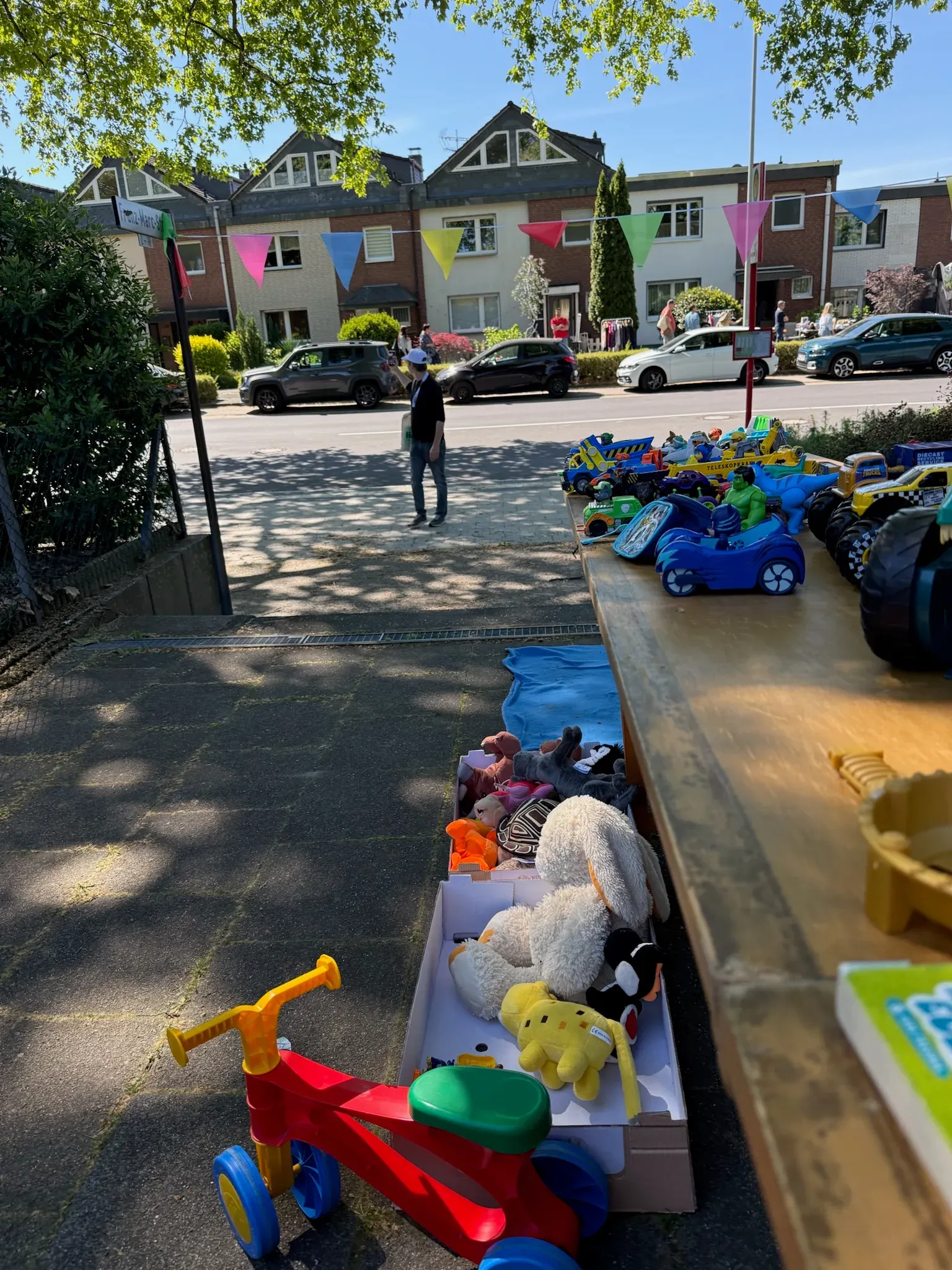 Tisch mit Spielzeugautos, daneben eine Kiste Kuscheltiere und ein Rutschrad, über der Straße Wimpel