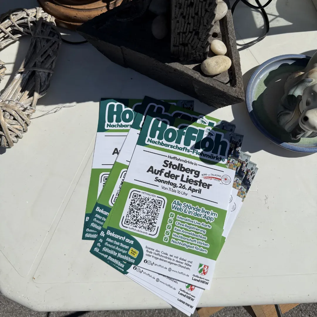 Stapel HofFloh-Flyer „Stolberg Auf der Liester, Sonntag, 26. April“ auf einem Tisch mit Deko